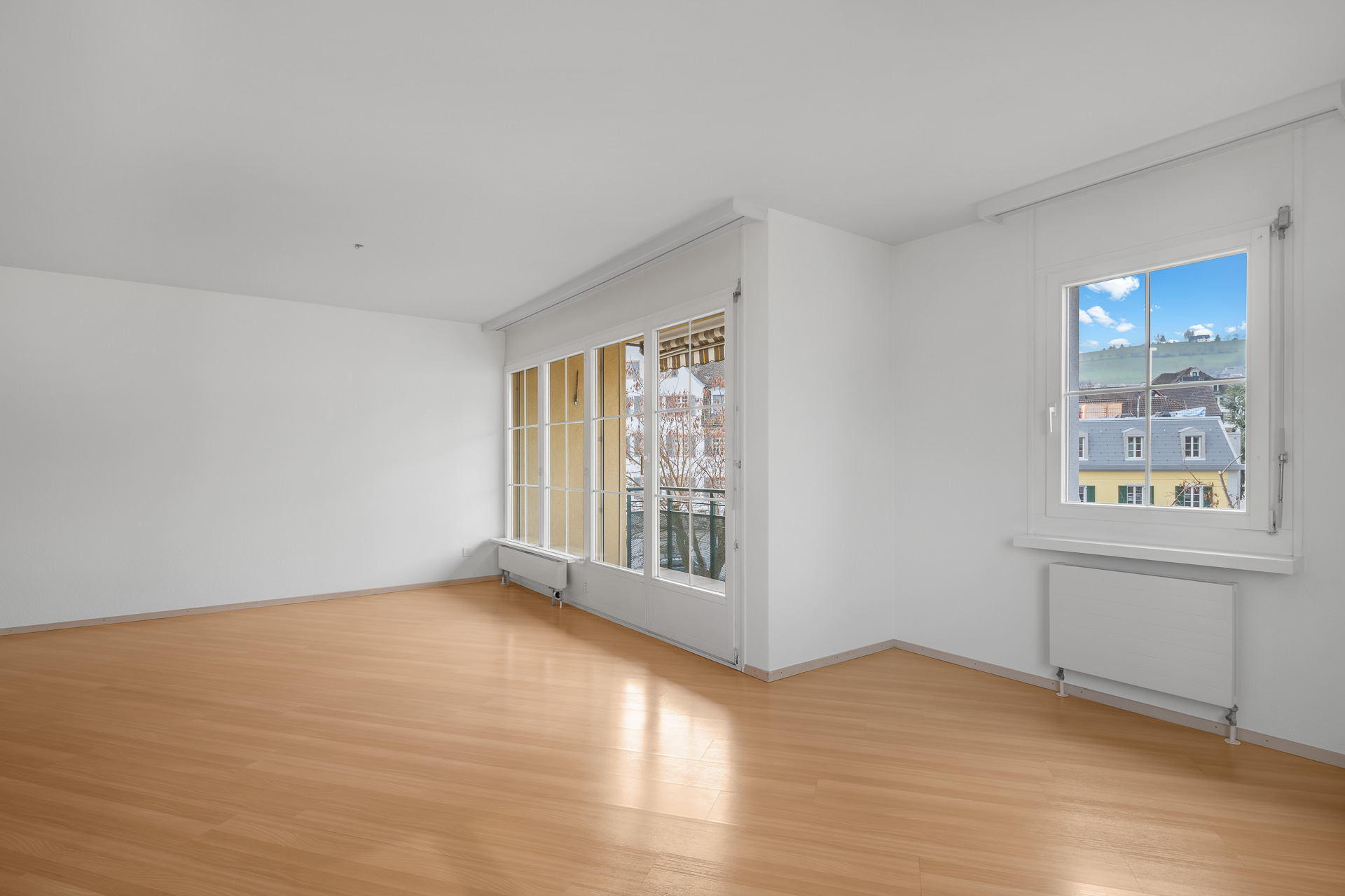 Heller leerer Wohnraum mit großen Fenstern und Blick ins Grüne