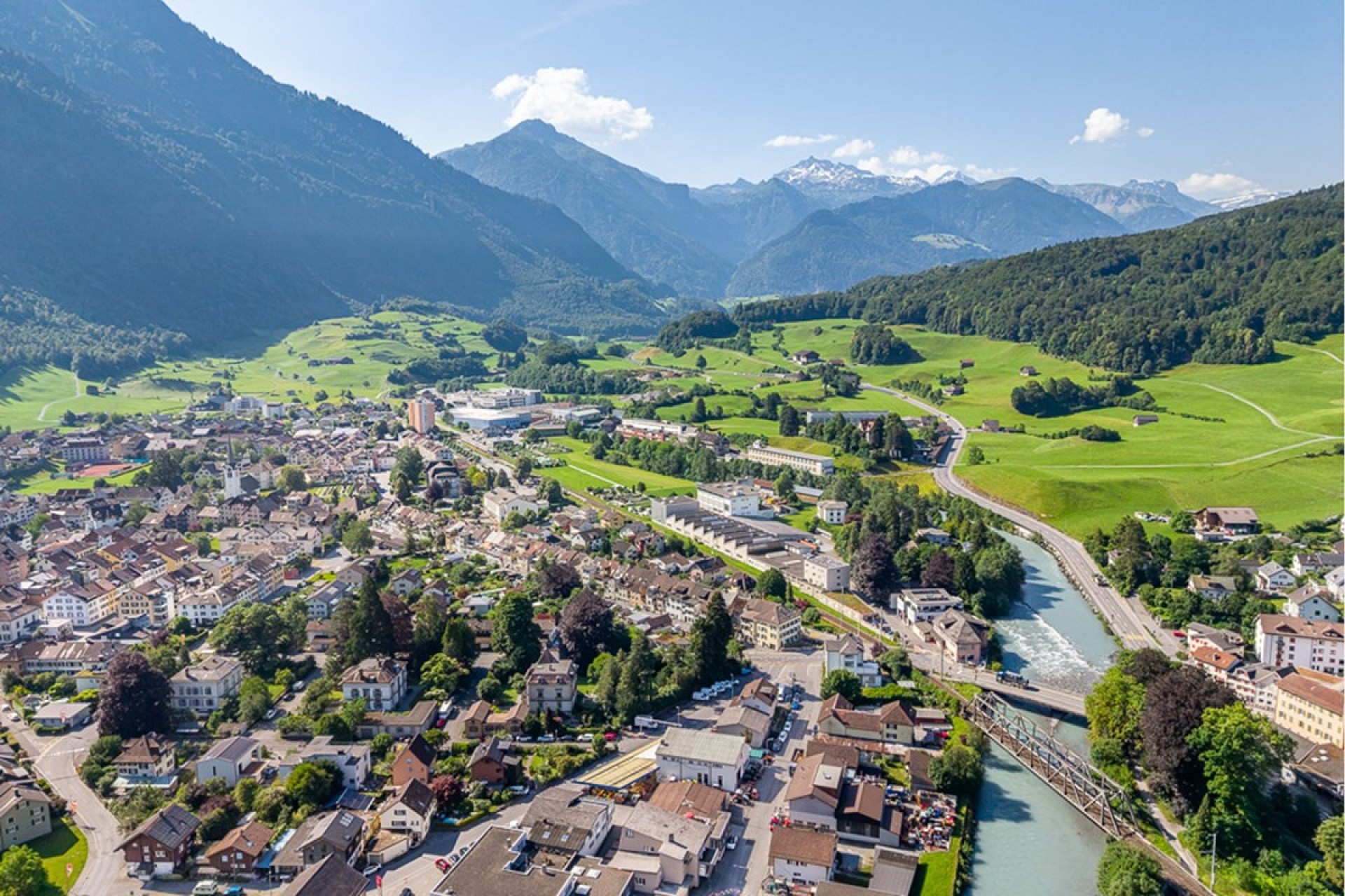 Luftaufnahme einer alpinen Kleinstadt mit Fluss und Bergpanorama