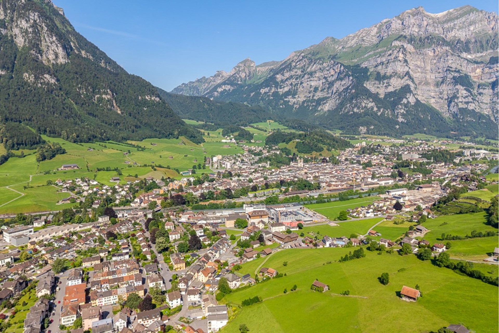 Luftaufnahme eines alpinen Tals mit Stadt und Bergen
