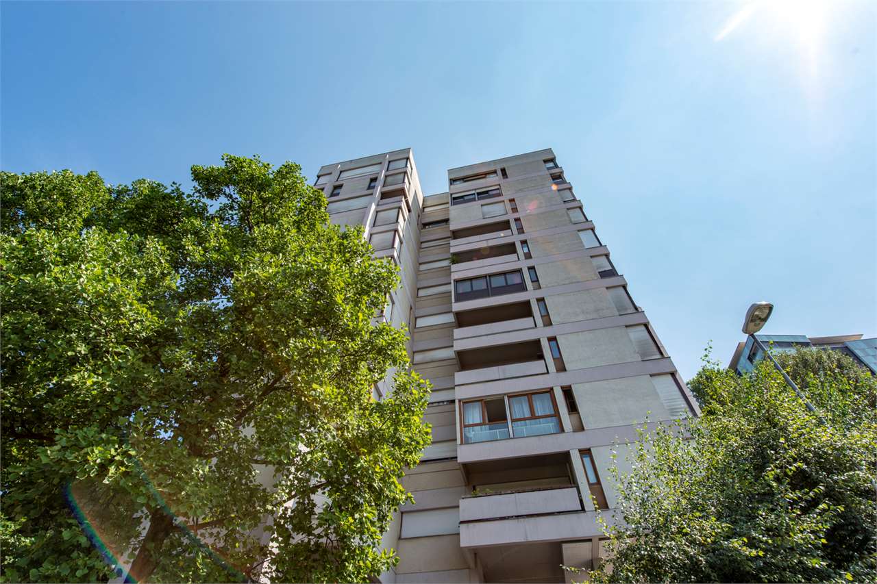 Mehrfamilienhaus von unten mit Bäumen und wolkenlosem Himmel