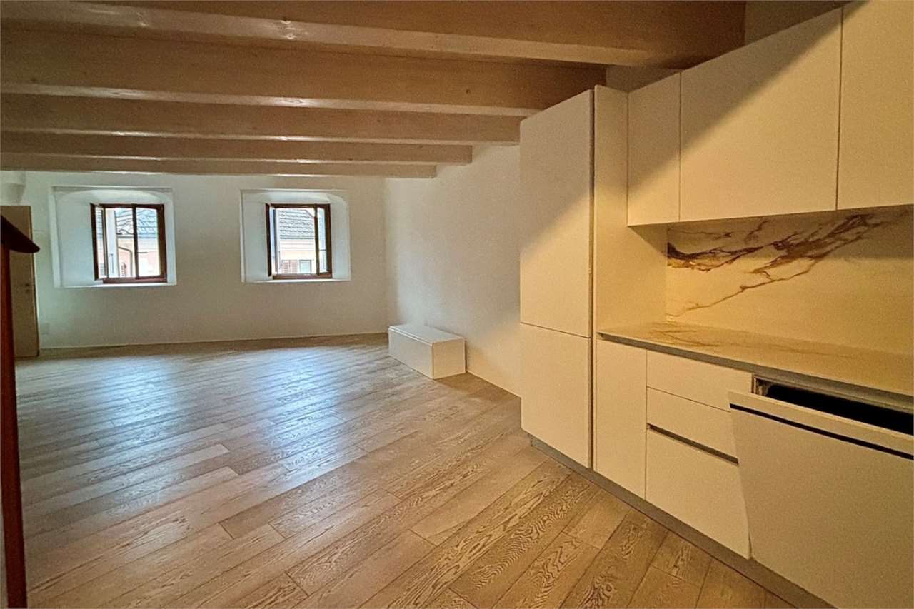 Heller, leerer Wohnraum mit Küche und Holzbalkendecke