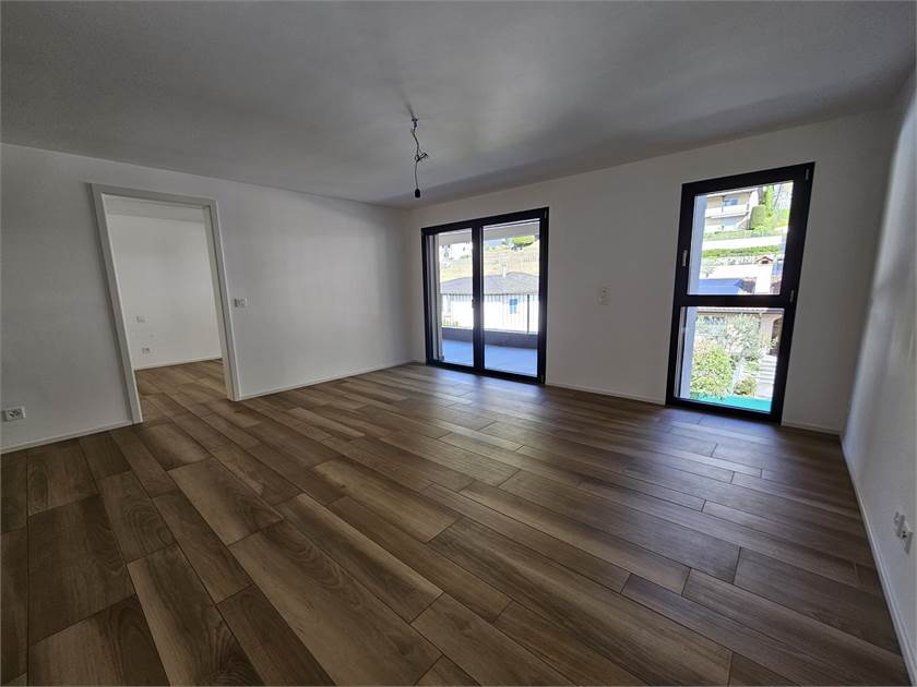 Leerer Wohnraum mit dunklen Fenstern und Holzoptikboden