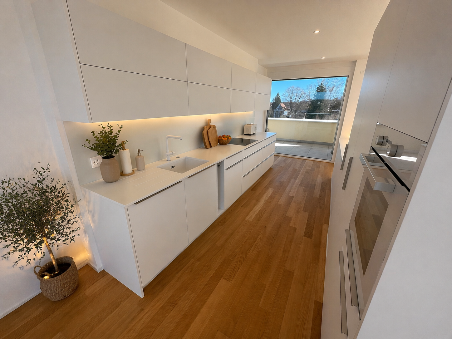 Moderne weiße Küche mit Holzfußboden und Balkonblick