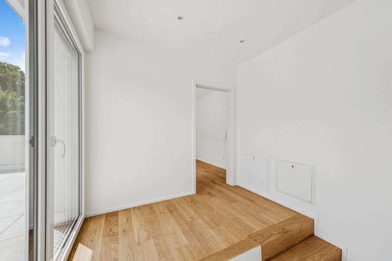 Heller leerer Raum mit großer Glastür und Holzstufe