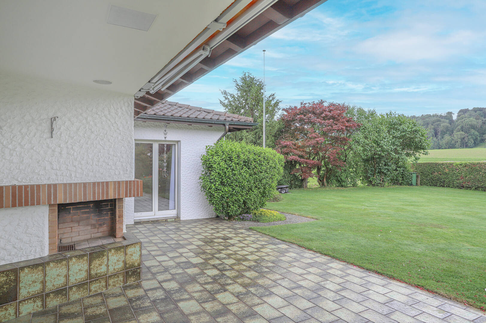 Überdachte Terrasse mit Grill und Gartenblick