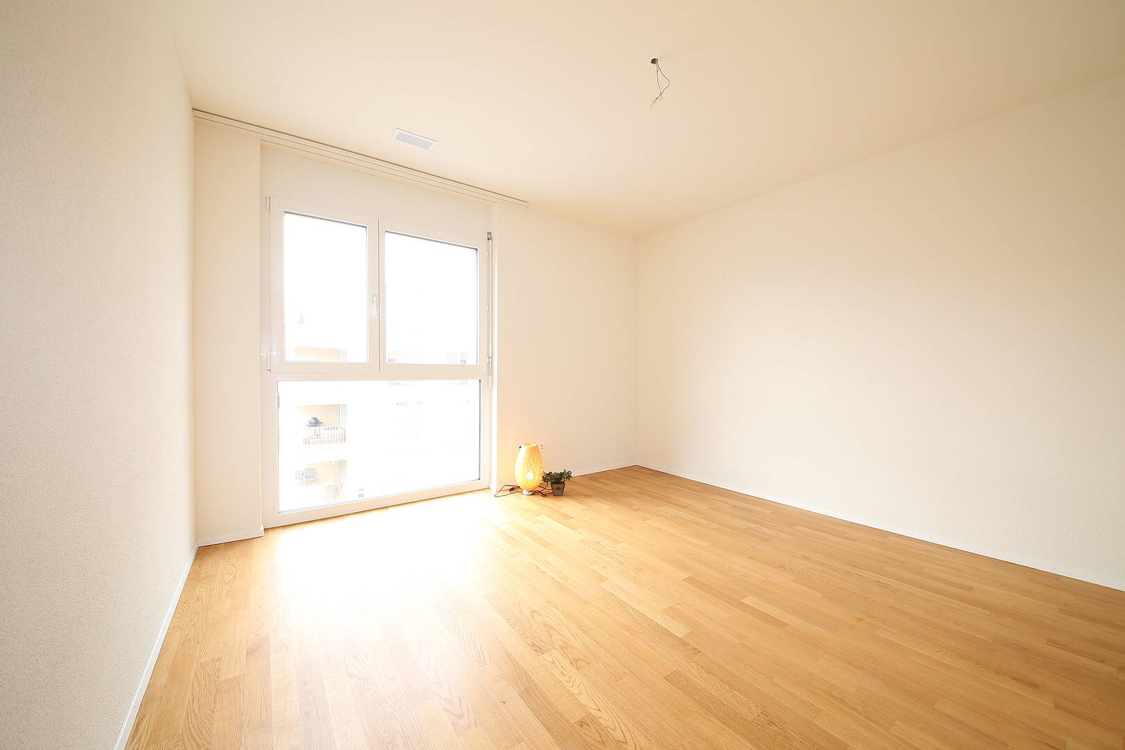 Heller, leerer Raum mit Parkettboden und großem Fenster