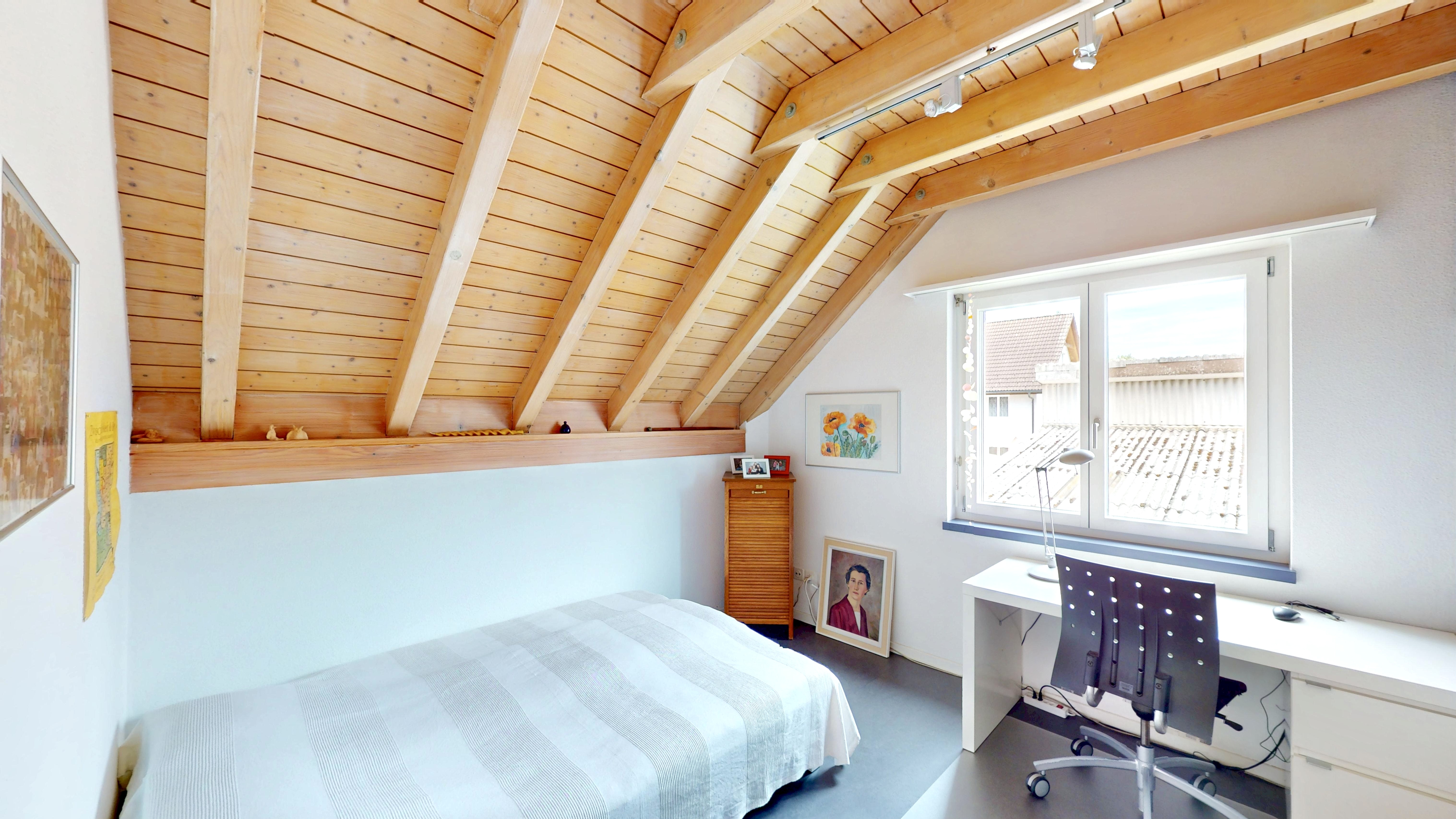 Helles Dachzimmer mit Bett und Arbeitsplatz