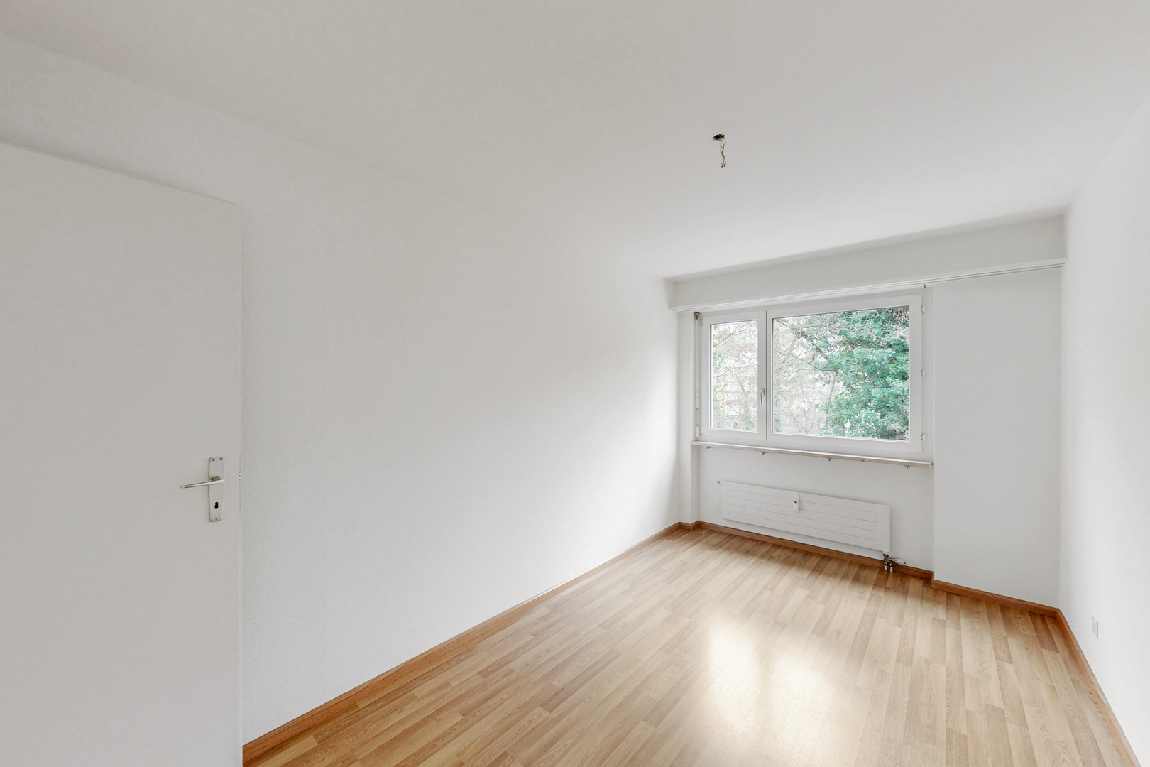 Helles, leerstehendes Zimmer mit Fenster und Holzboden