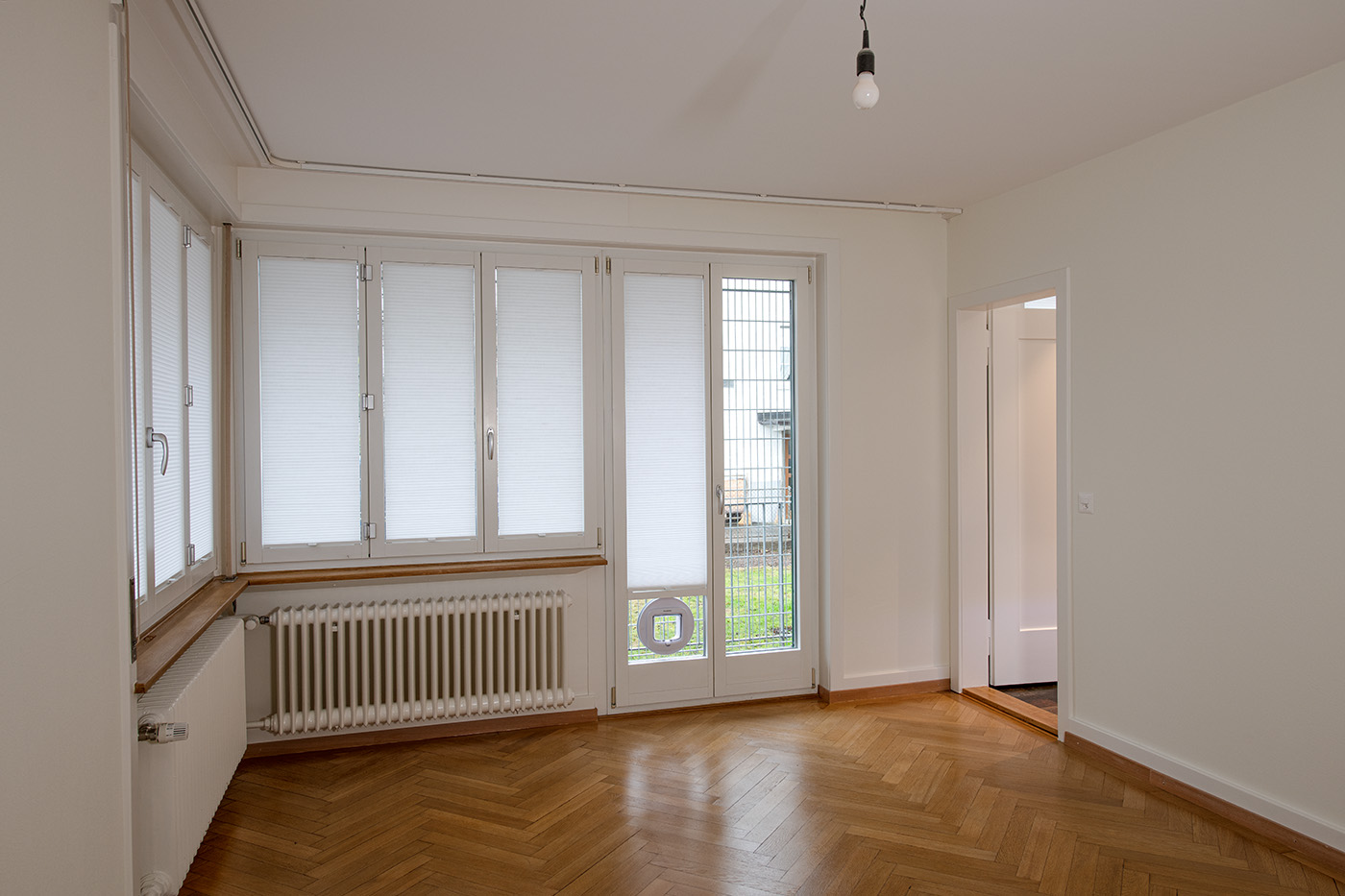 Heller leerer Wohnraum mit Parkett und großen Fenstern