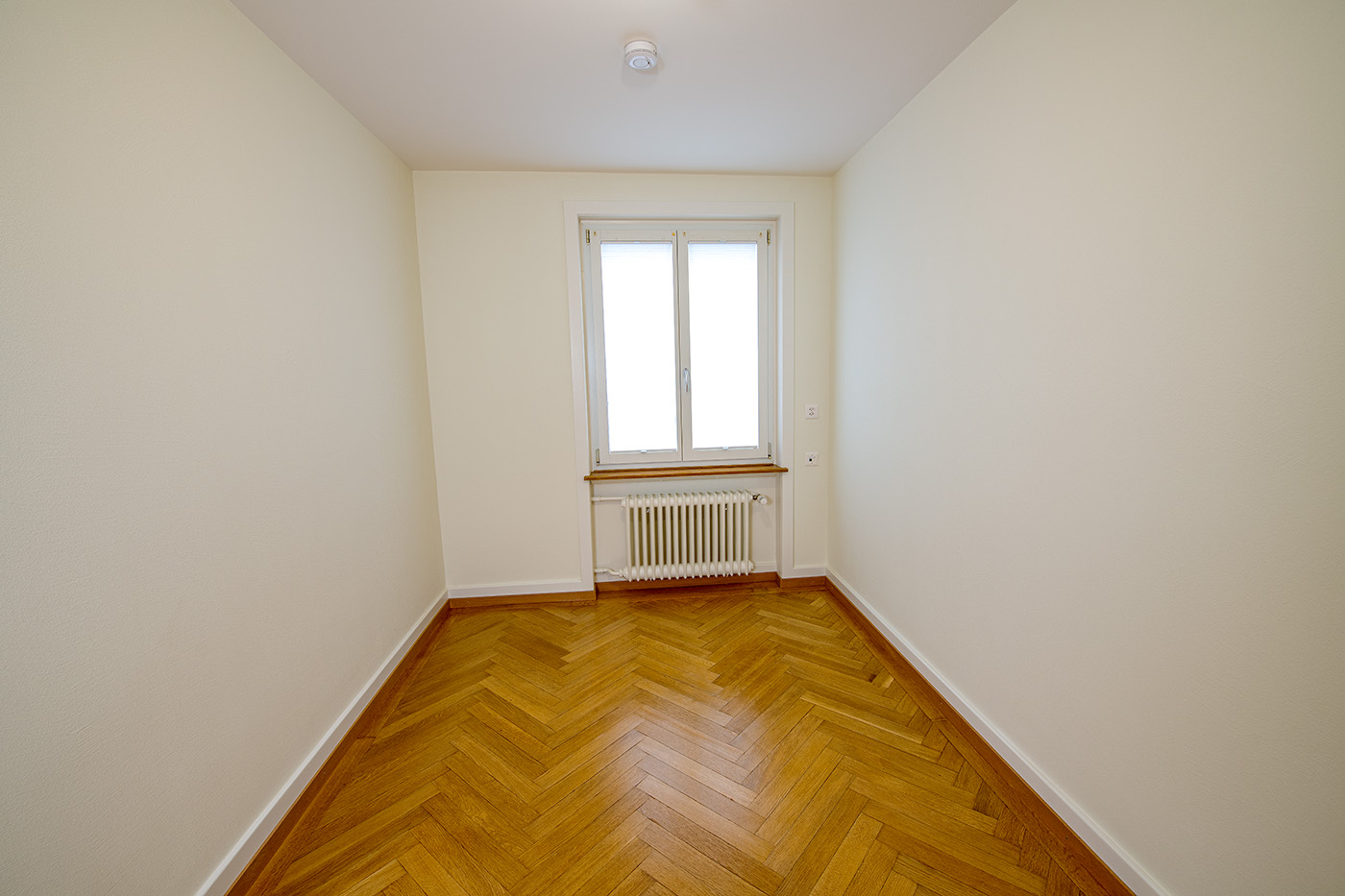 Schmaler leerer Raum mit Parkett und Fenster