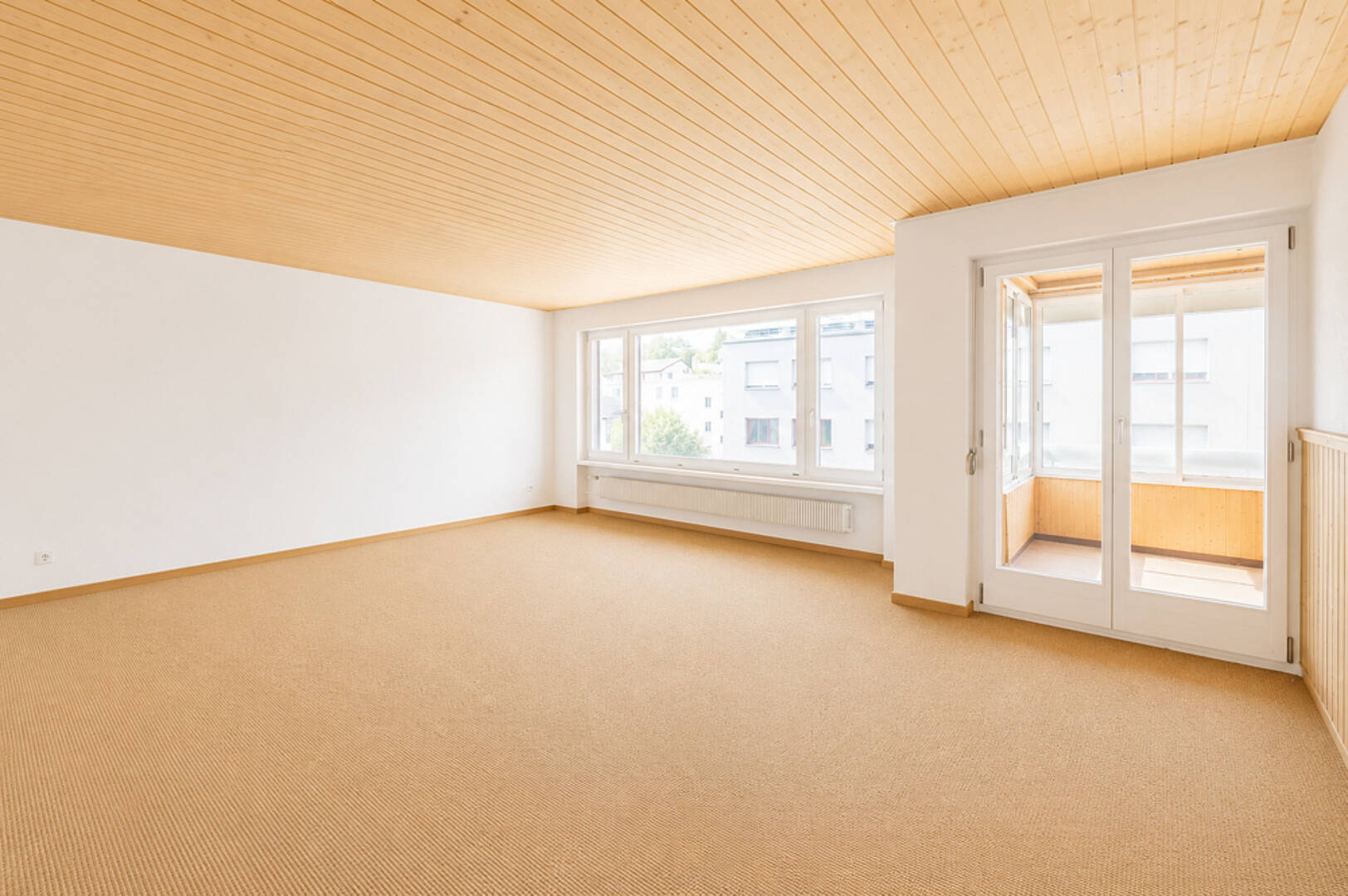 Heller leerer Wohnraum mit großem Fenster und verglaster Tür zum Balkon