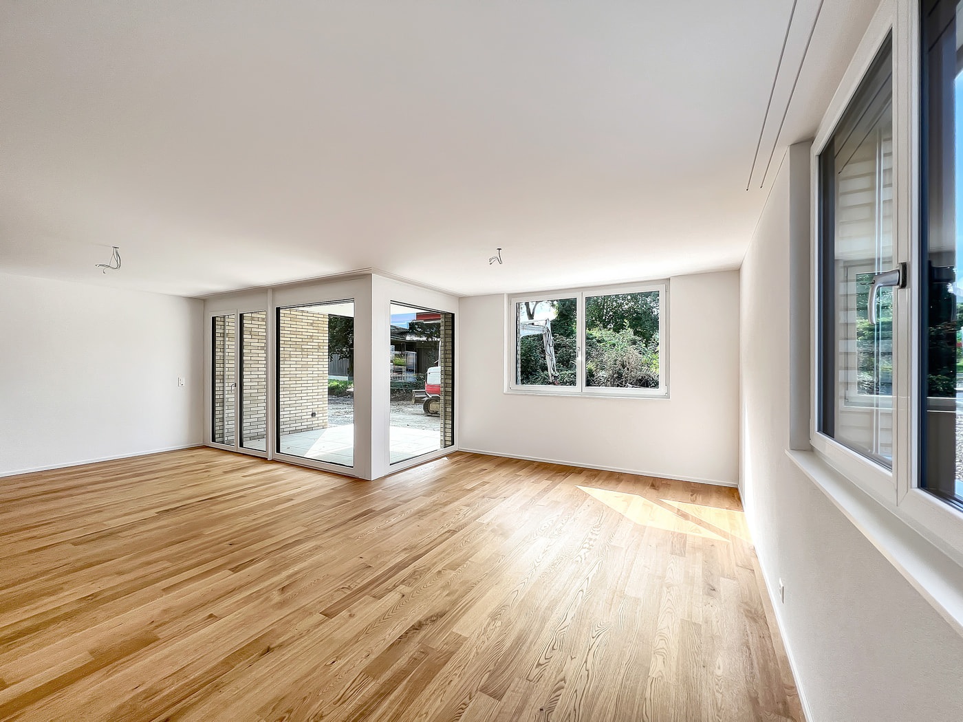 Heller leerer Wohnraum mit Holzfußboden und großen Fenstern