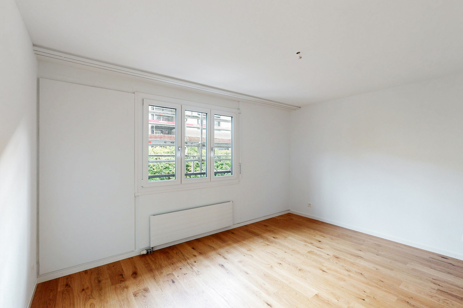 Helles, leeres Zimmer mit Holzboden und Fenster