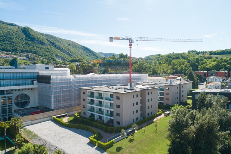 Außenansicht einer Wohnanlage mit Baustelle und Bergkulisse