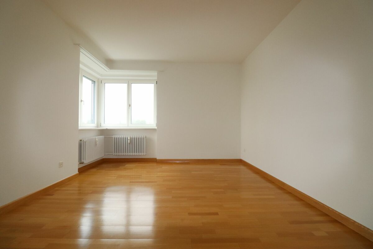 Leerer heller Wohnraum mit Parkett und Eckfenster