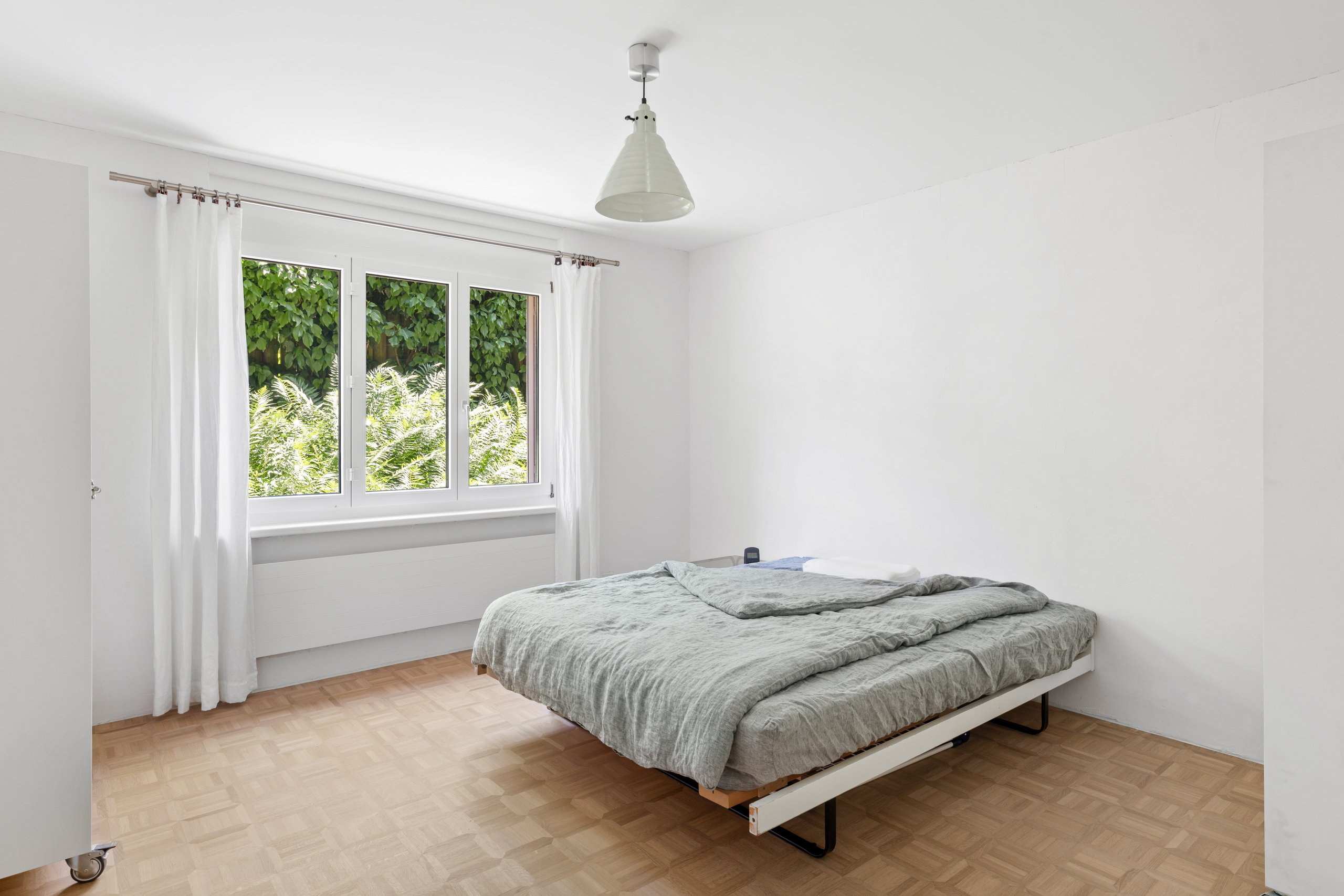 Helles Schlafzimmer mit Bett und Fensterblick ins Grüne