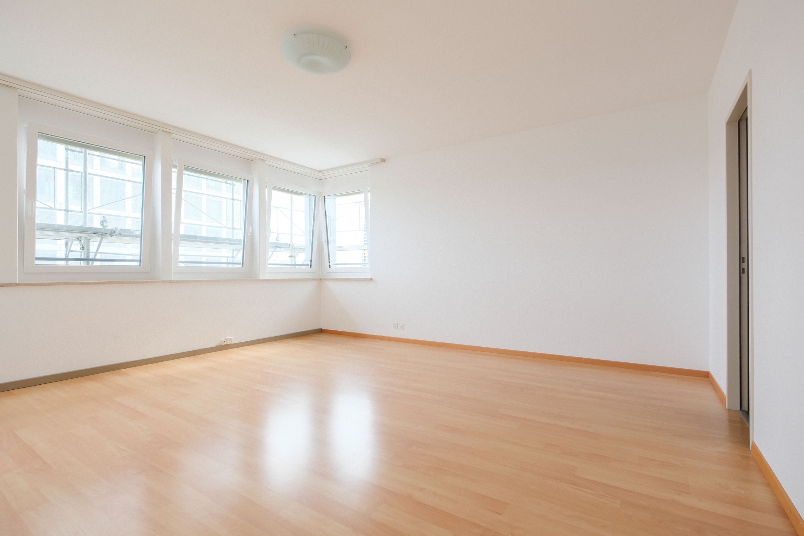 Leerer, heller Wohnraum mit Parkettboden und großen Fenstern