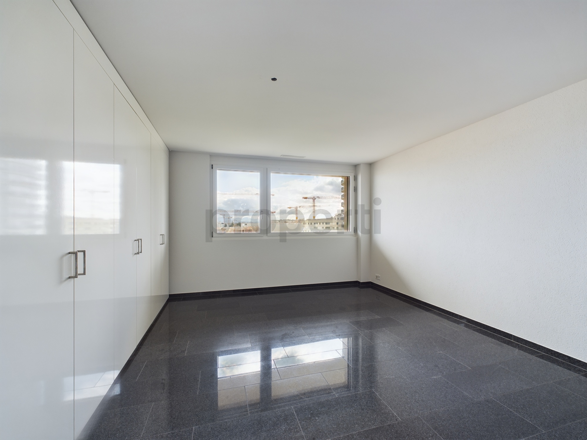 Helles, leeres Zimmer mit Einbauschrank und Fensterblick auf die Stadt