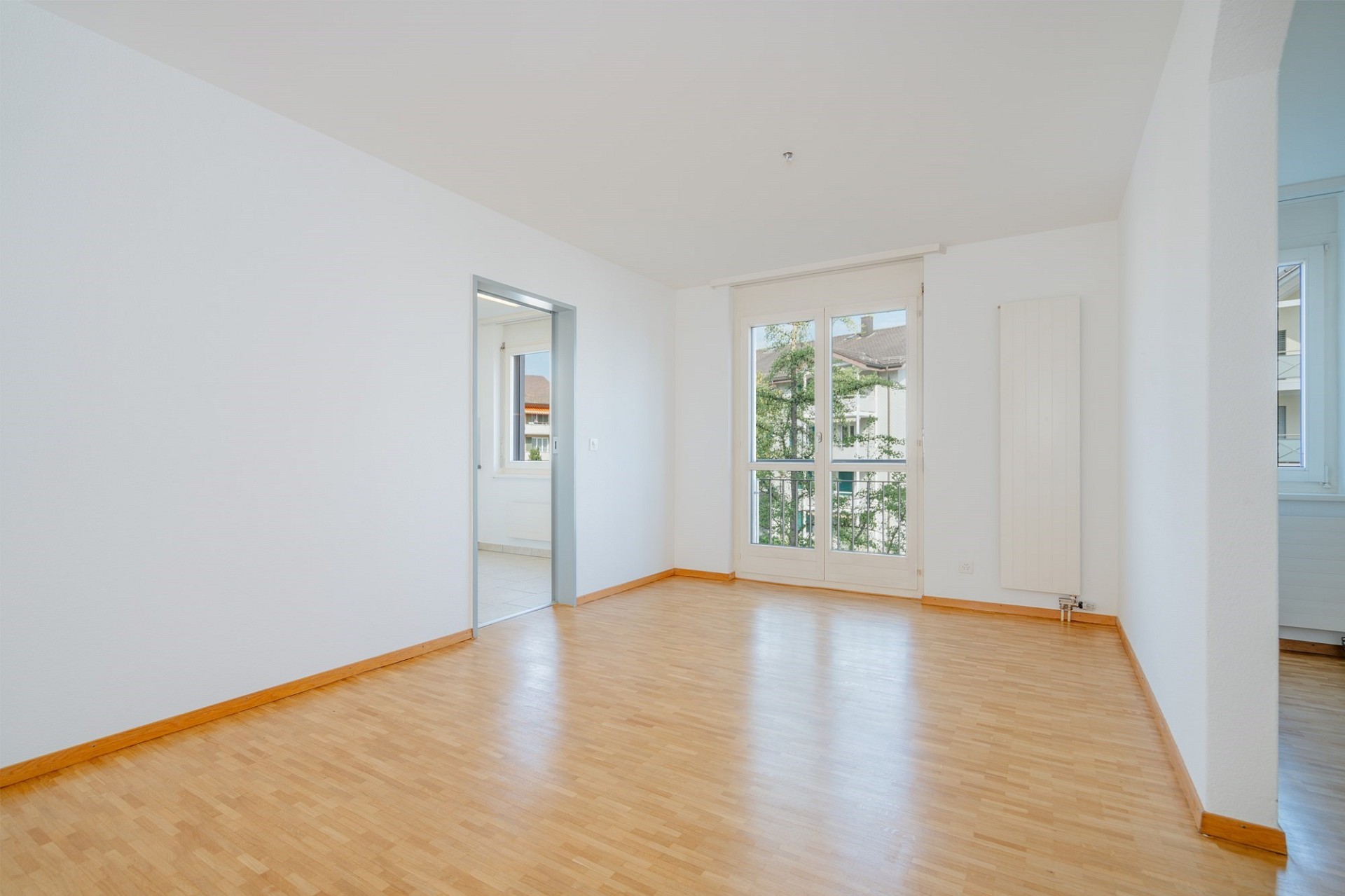 Heller leerer Wohnraum mit Parkettboden und Balkonfenster