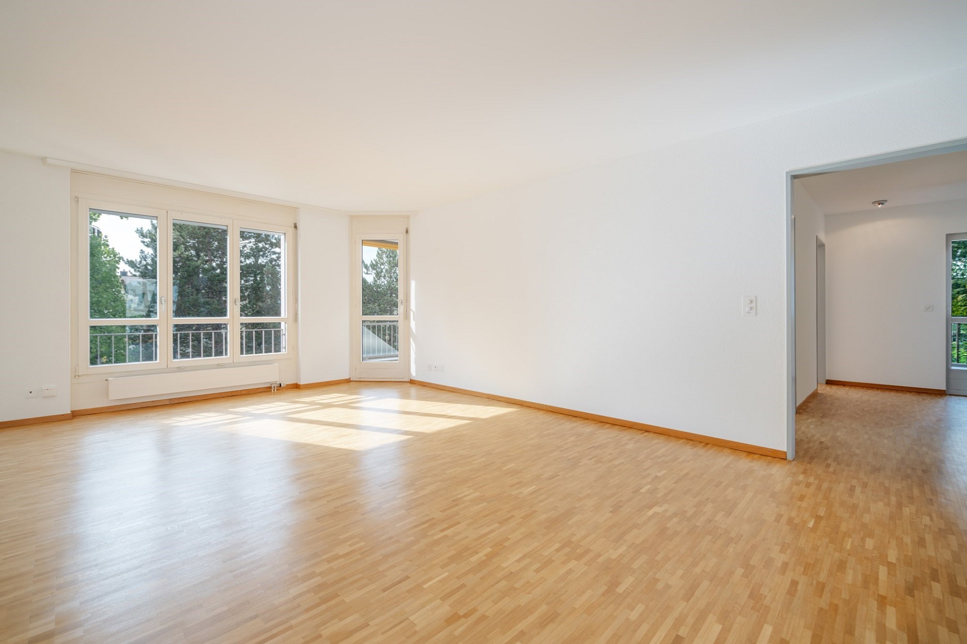 Heller leerer Wohnraum mit Parkett und Balkonblick