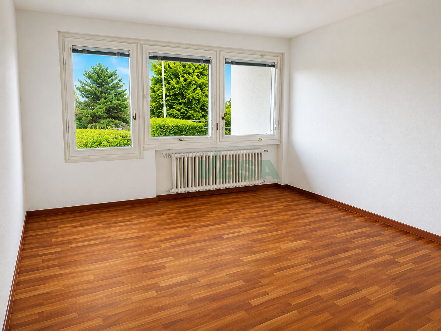 Leeres Zimmer mit Holzoptik-Boden und Blick ins Grüne