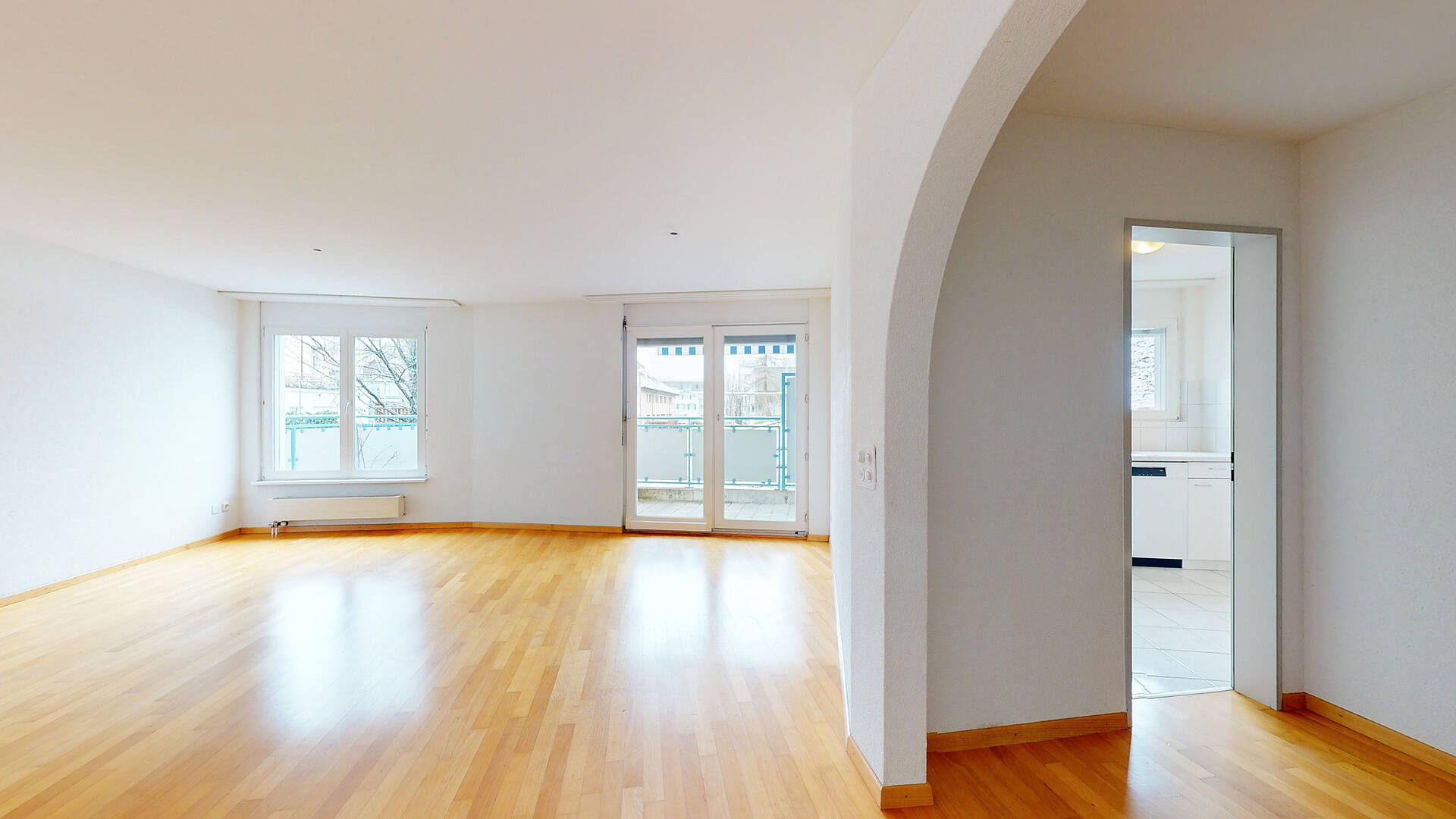 Heller Wohnraum mit Balkon und offener Durchgangsöffnung zur Küche