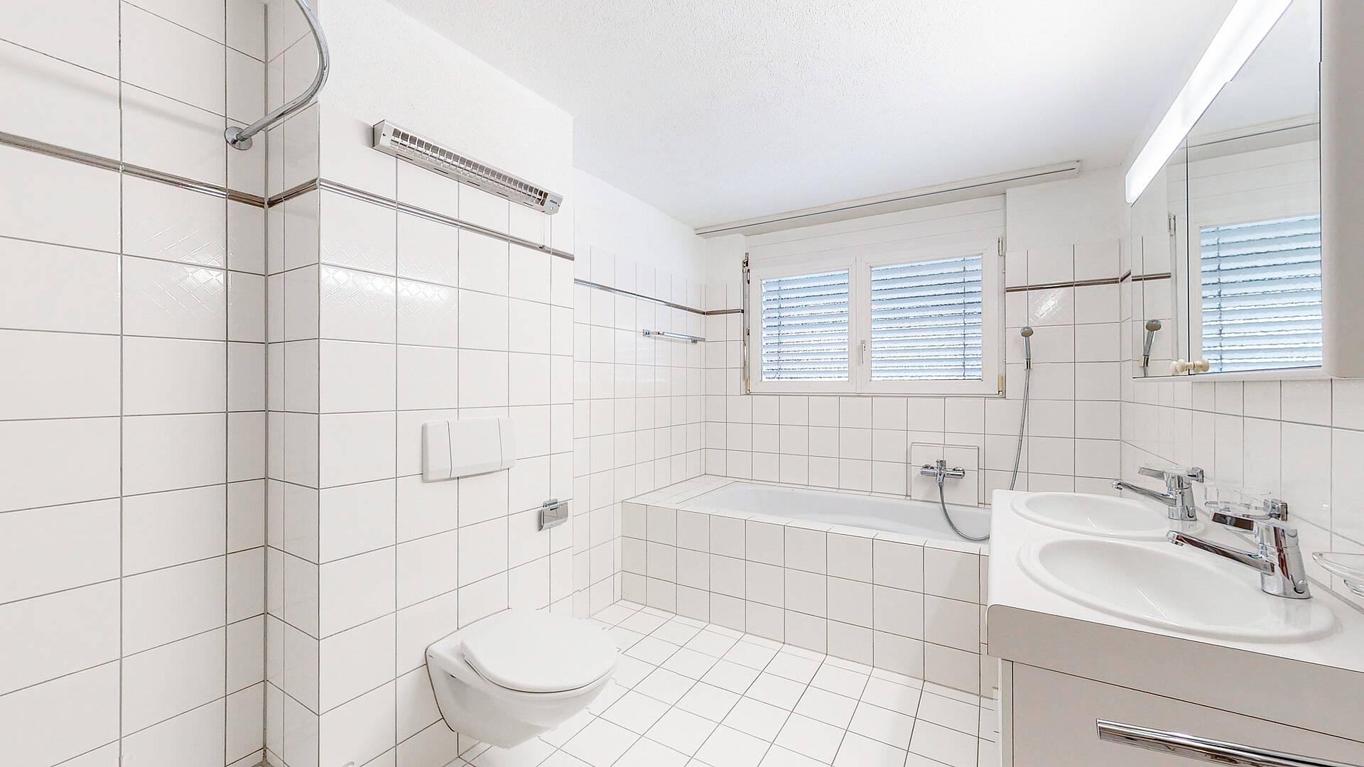 Helles, weiß gefliestes Badezimmer mit Wanne, Doppelwaschtisch und WC