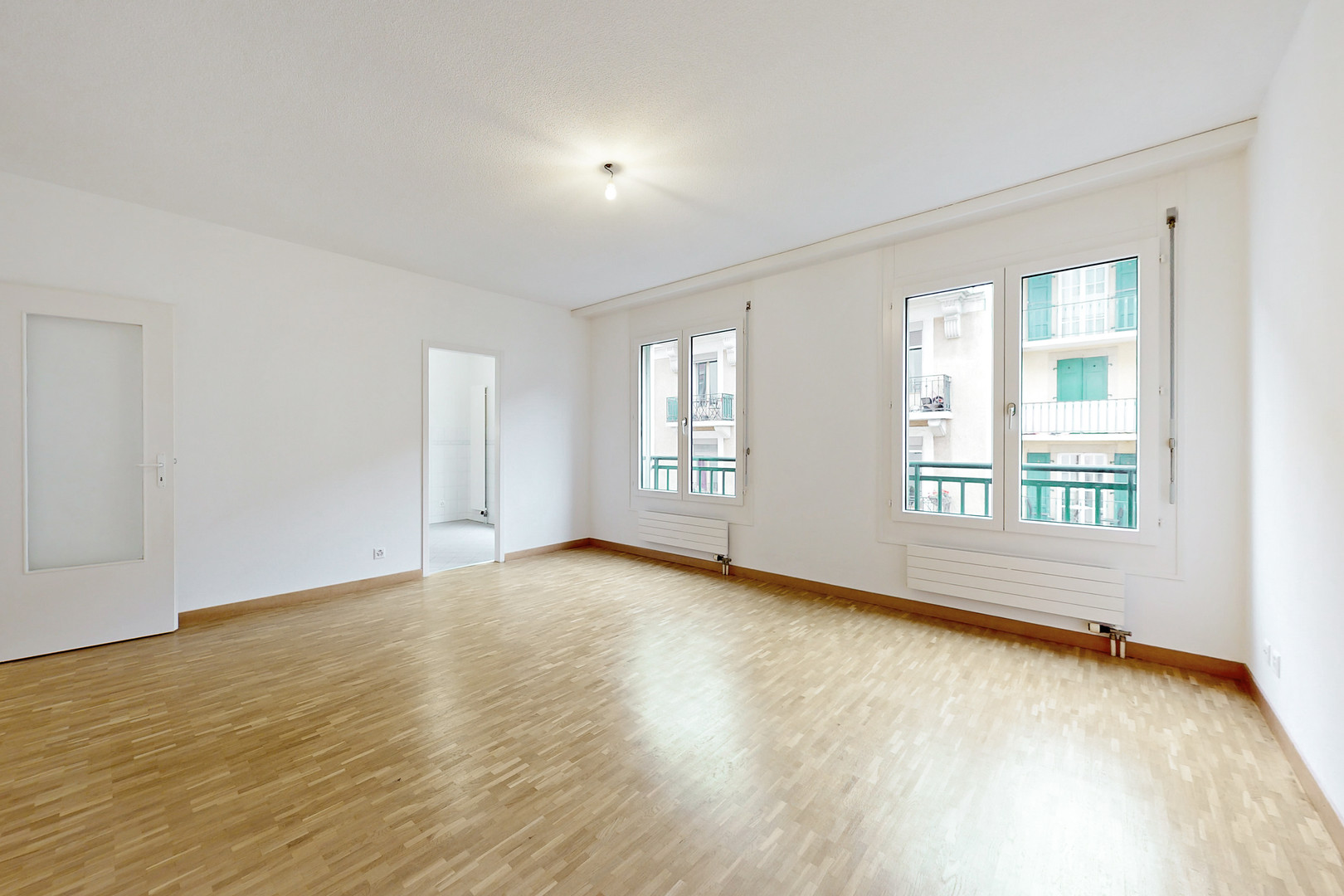 Helles, leeres Wohnzimmer mit Parkett und großen Fenstern