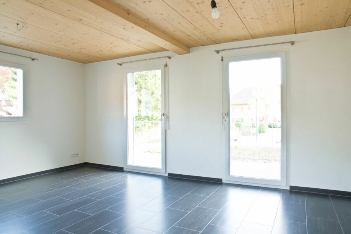 Heller leerer Raum mit Holzbalkendecke und großen Fenstertüren