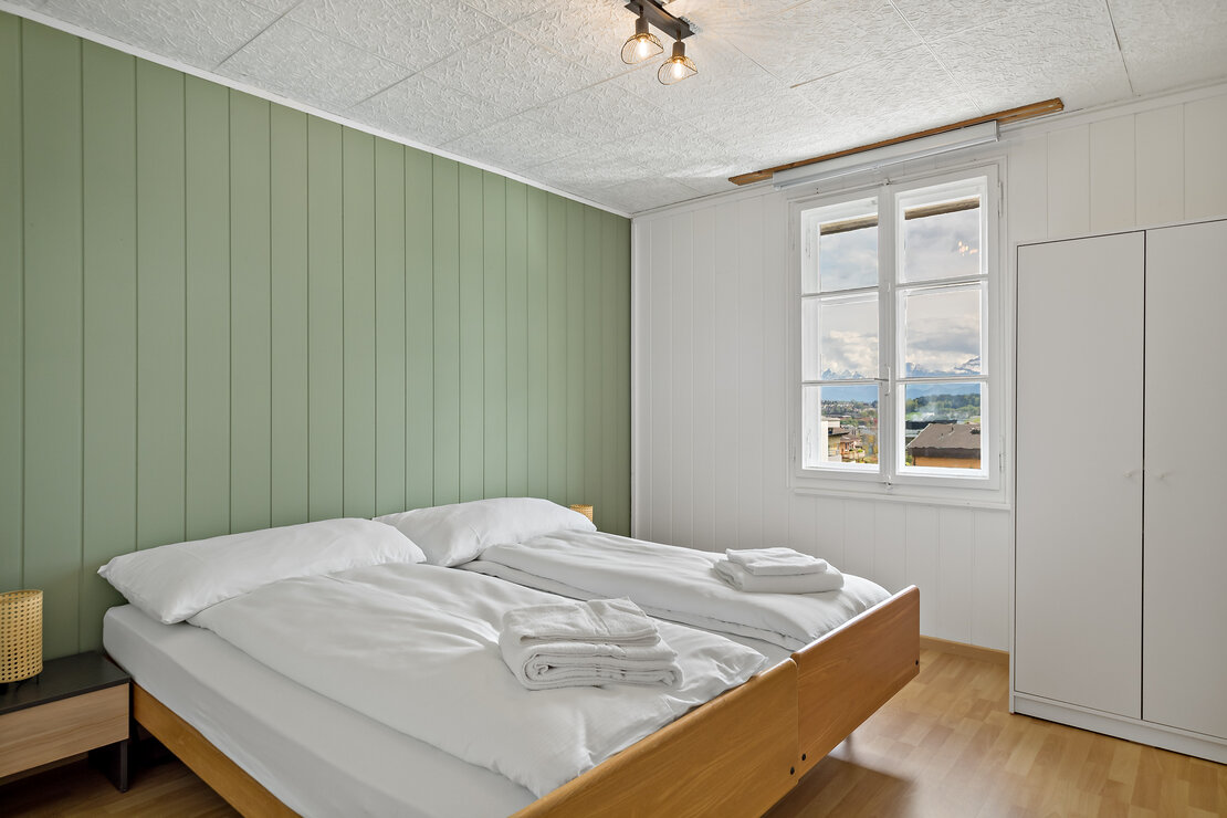 Helles Schlafzimmer mit grüner Akzentwand und Blick ins Freie