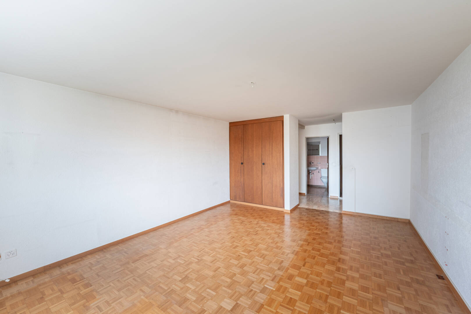 Leerer Wohnraum mit Parkettboden und Einbauschrank
