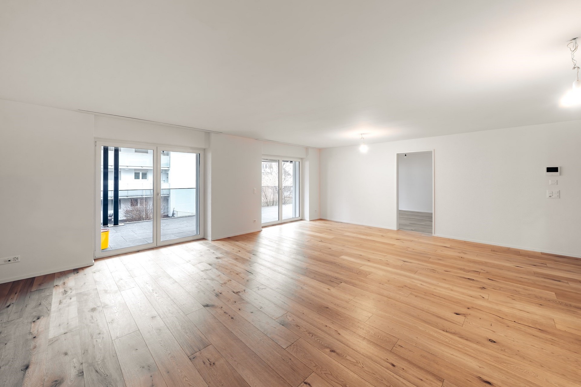 Heller, leerer Wohnraum mit Holzparkett und großen Fenstern